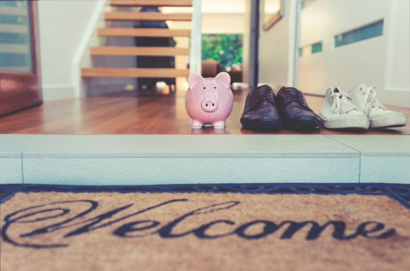 Saving for a new home concept. Piggy bank standing at front door
